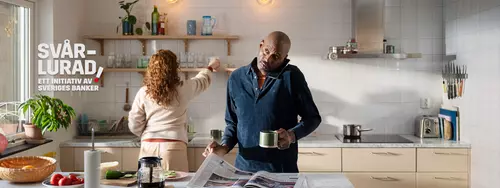 En man läser tidningen, pratar i telefon och dricker kaffe samtidigt.