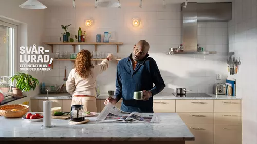 En man läser tidningen, pratar i telefon och dricker kaffe samtidigt.